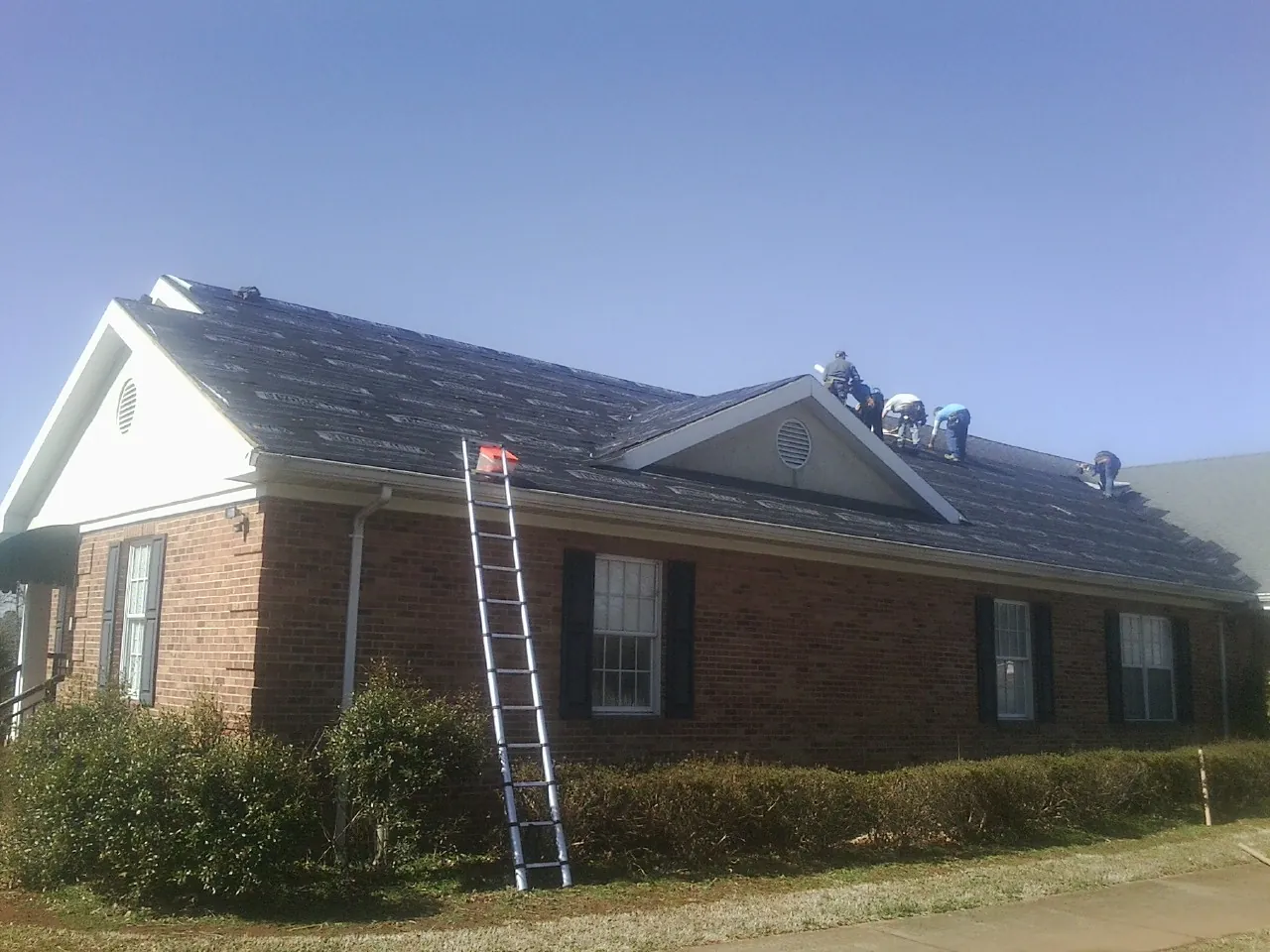Crew tearing shingles off a brick ranch roof with a ladder set — Metal Roof Repair work by our crew in Robertsdale