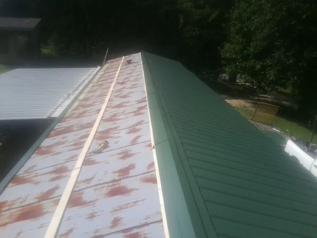 Old rusted panels beside newly installed green metal roofing — Wind Damage Roof Repair by Roofing Brothers in Robertsdale