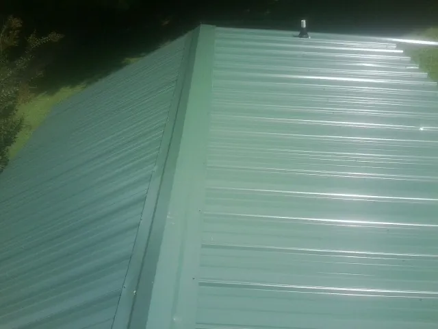New green metal panels meeting at the ridge of a roof — Flat Roof Repair work by our crew in Robertsdale
