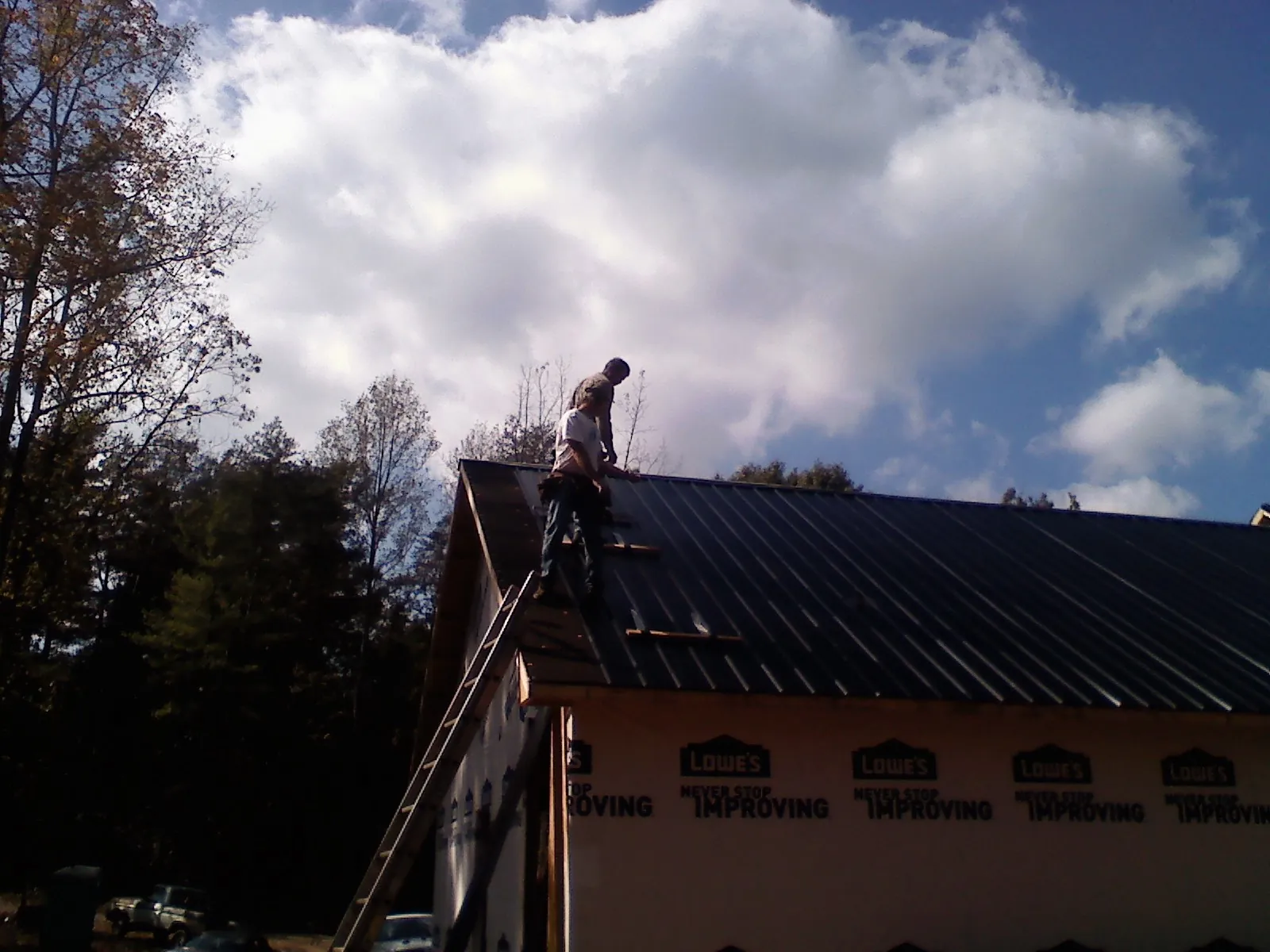 Roofer fastening dark metal panels high against a cloudy sky, from a Roof Inspection job in Robertsdale