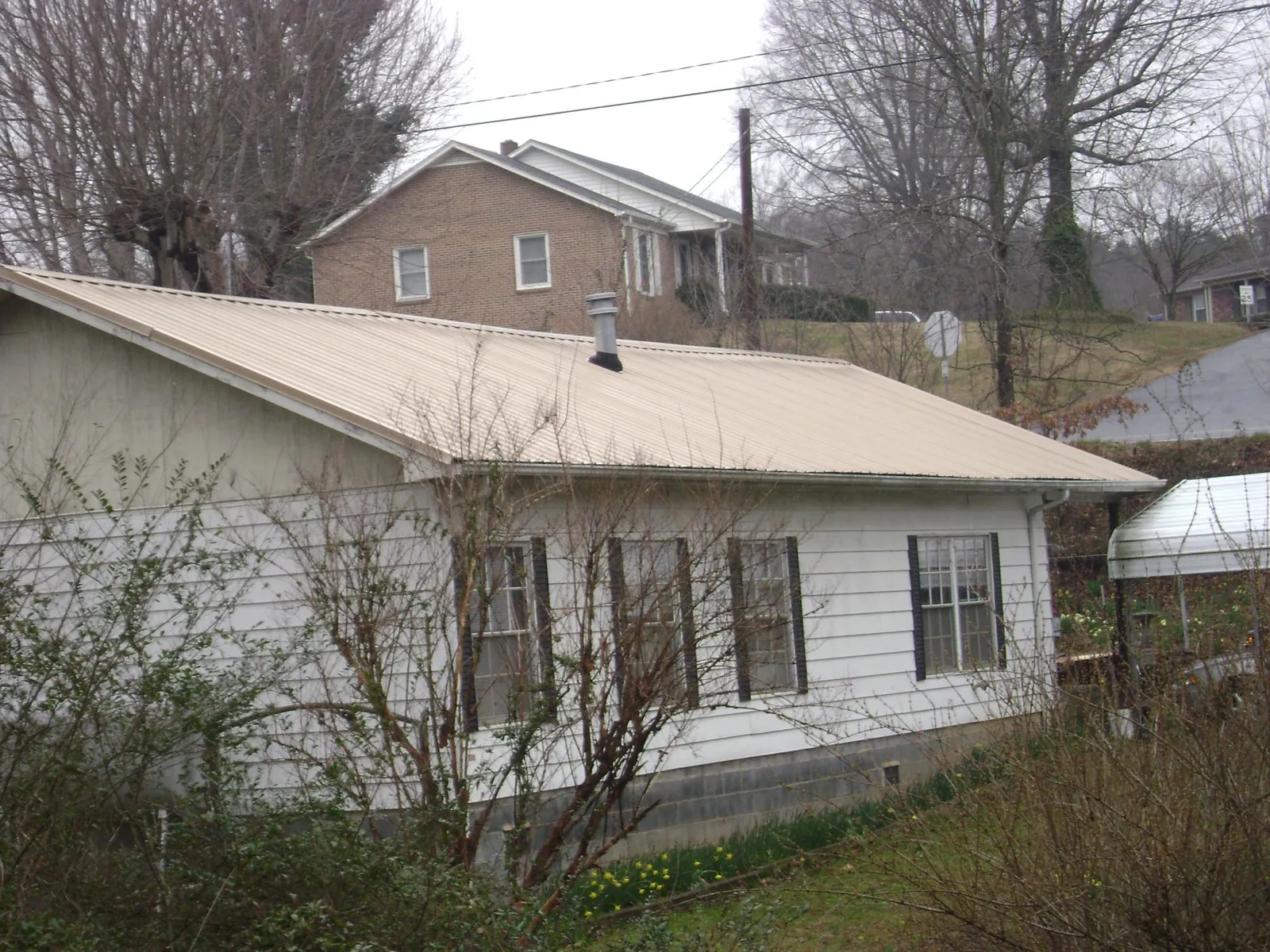 Tan metal roof on a white sided house set into a hillside — Commercial Roofing by Roofing Brothers in Robertsdale