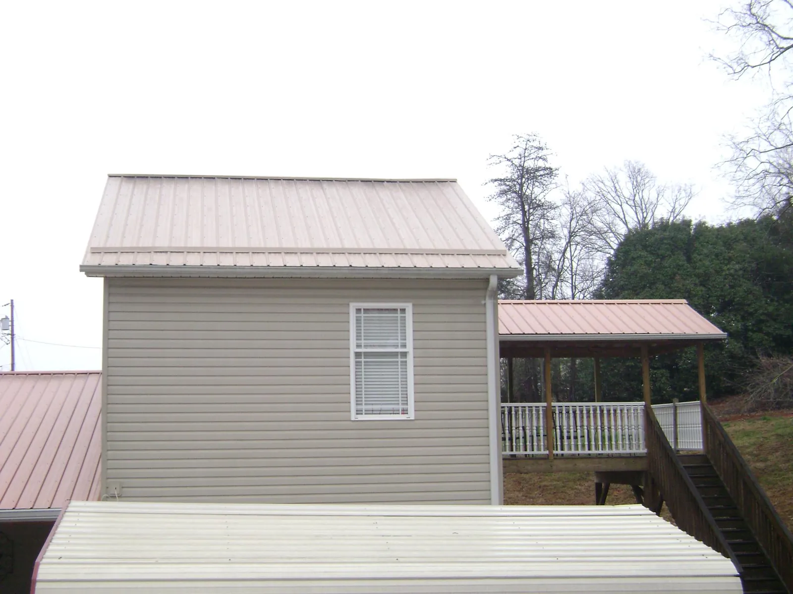 Tan metal roofs on a two story addition and attached porch, from a Roof Replacement job in Robertsdale